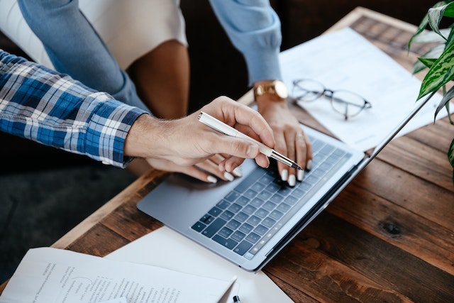 A landlord leans over their laptop while a colleague points out a typo in their property listing on the laptop screen