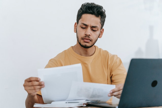 a property manager with short black hair and a close cropped beard reviews tenant applications at their desk while wearing a yellow crewneck sweater